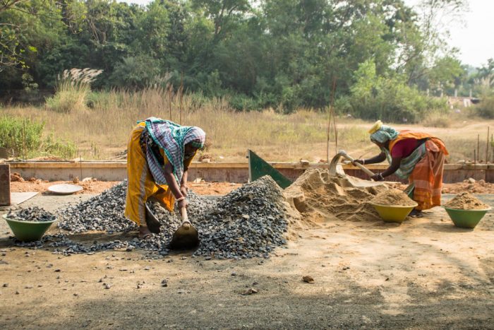 Laborers are working around concrete batch mixer in India.