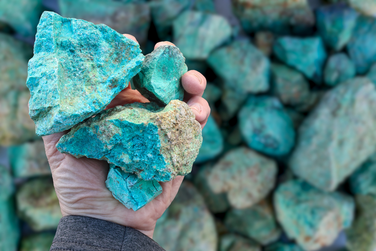Blue green copper (Cu) oxide ore, held in hand, against background of ore that is out of focus. Mining.
