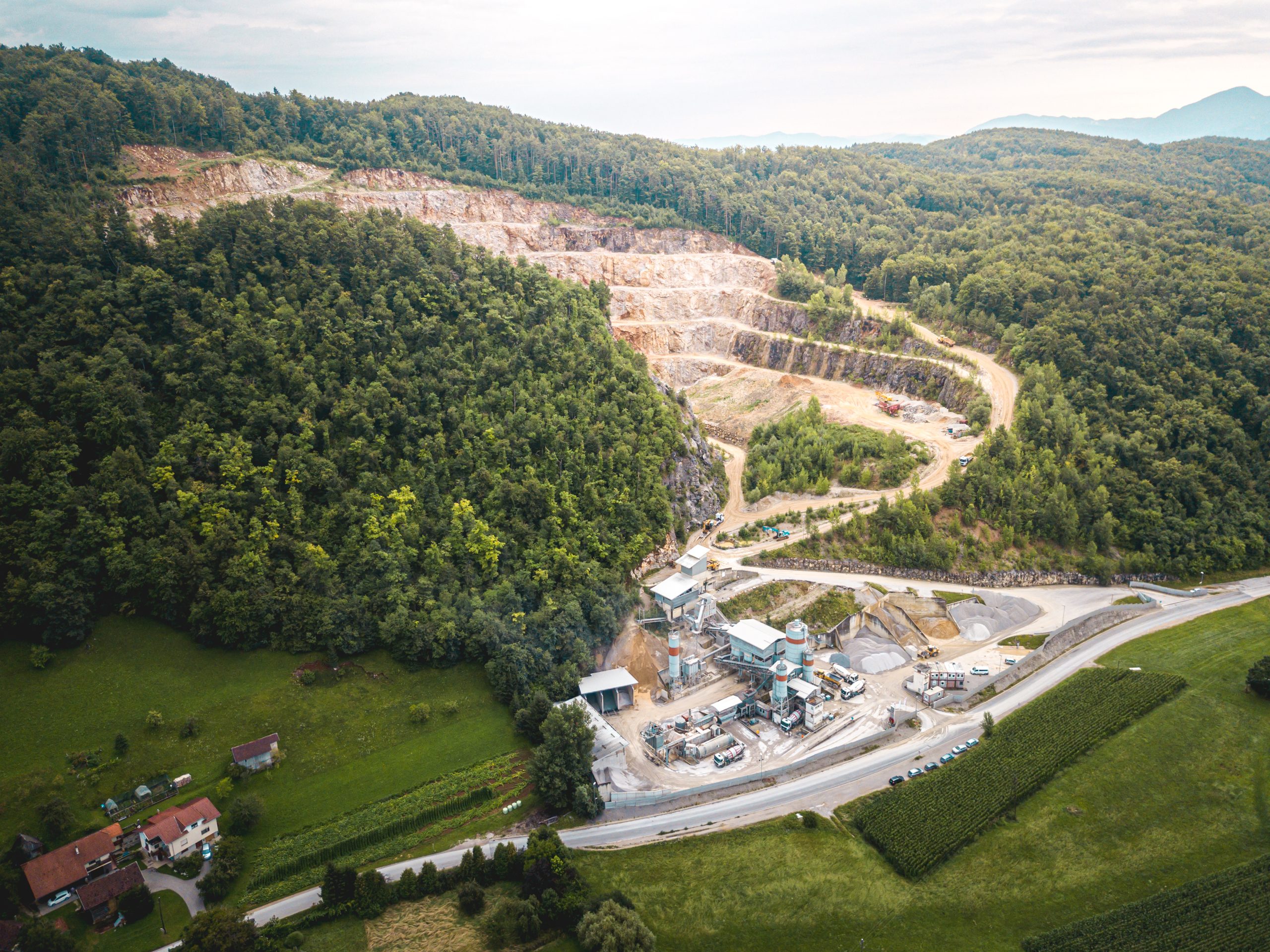 Aerial view of mining plant with quarry, surrounded by forest and green fields.